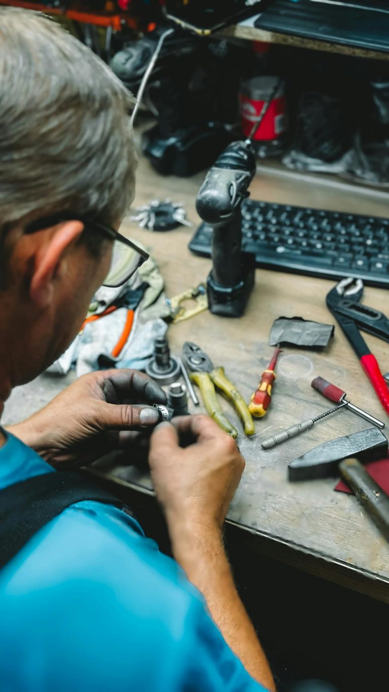 A worker focused on repairing tools at a cluttered workshop desk, showcasing handiwork and craftsmanship.